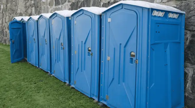 Row of blue portable toilets lined up on grass against a stone wall for event sanitation in Arvada, CO