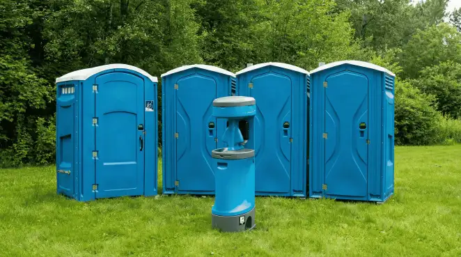 Four blue portable toilets and a matching hand washing station on grass near trees, a common sight at local outdoor events in Arvada, CO