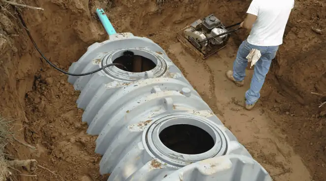 Septic tank installation showing a technician compacting soil around a new poly septic tank in an excavation pit in Arvada, CO